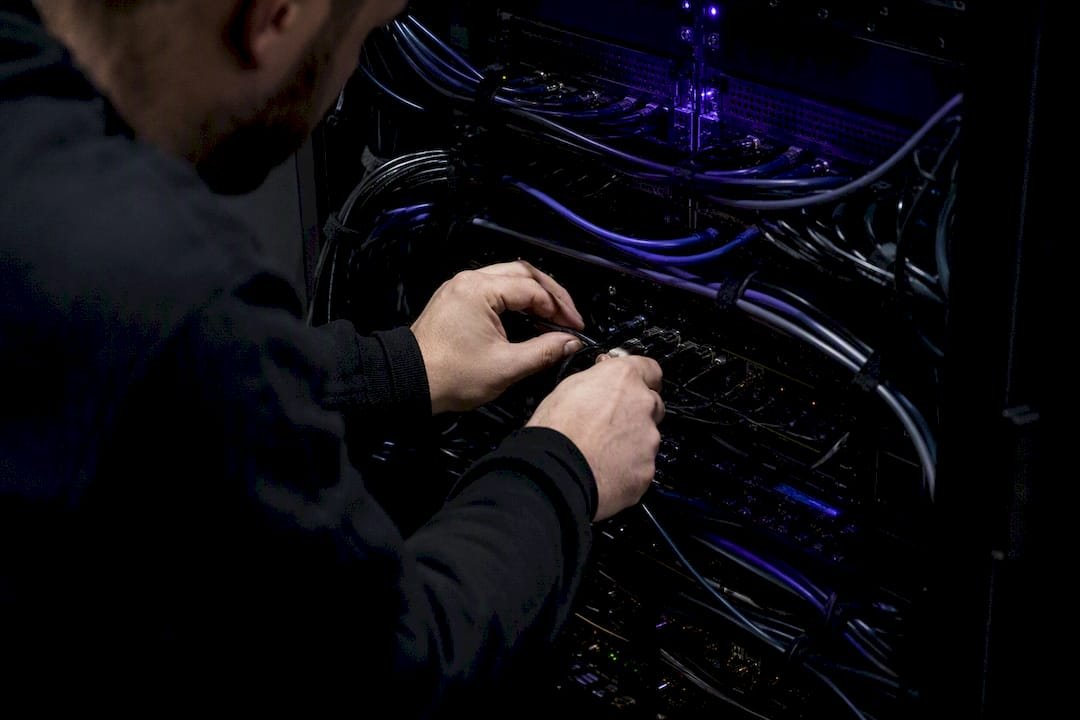 Specialisto rankos jungia serverių kabelius modernioje technologijų dirbtuvėje.